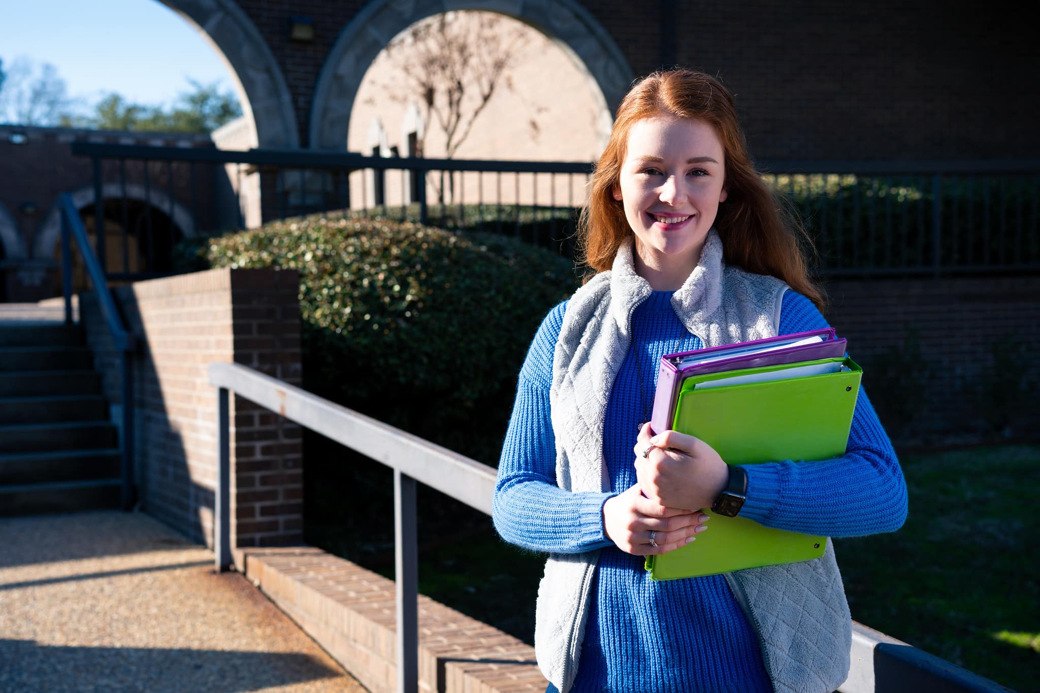 college student standing in front of academic building holding class materials