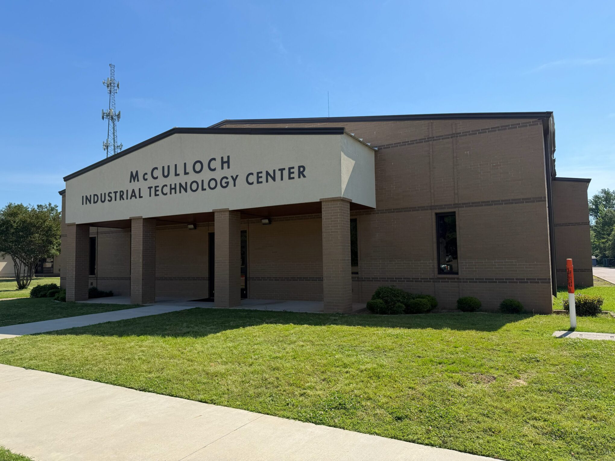 A brick building with a covered entrance labeled McCulloch Industrial Technology Center stands on a grassy lawn under a clear blue sky.