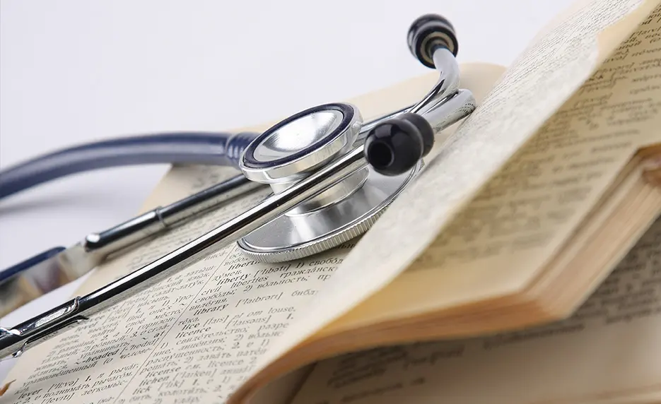 A stethoscope rests on the open pages of a book, symbolizing the connection between medicine and learning.