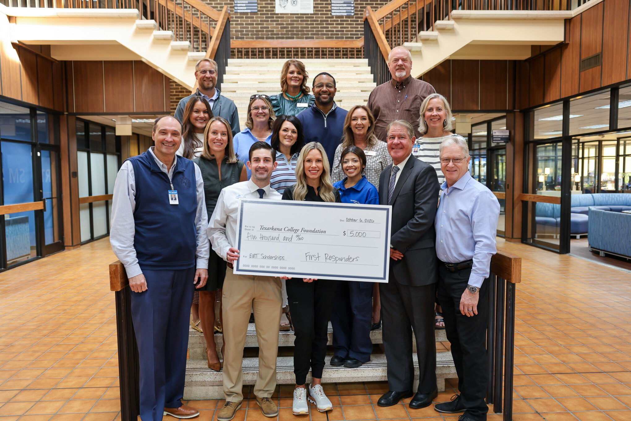 A large group of people standing on a staircase holding a $5,000 ceremonial check from the Texarkana College Foundation for EMT scholarships.