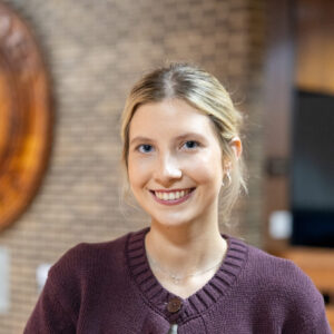 A smiling young woman wearing a button-down maroon cardigan.